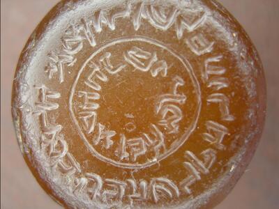 Photo of a circular, translucent orange object with reversed Hebrew writing in concentric circles.