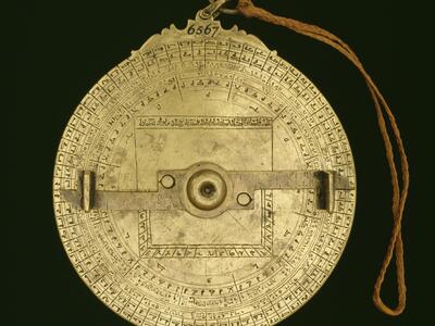 Circular, intricate brass object with Arabic and Hebrew inscriptions, geometric markings, and a rotating arm.