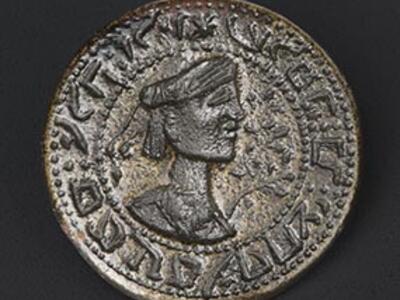 Round bronze seal with a turbaned bust in profile and floral decoration, encircled by reversed Hebrew text.
