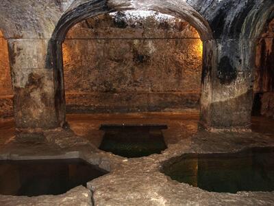 Photo of stone room with arched ceilings, pillars, rough walls, and several pointed pentagonal pools set into the floor.