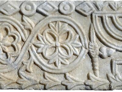 Stone relief with a candelabrum, horn, and plant bundle, floral patterns, and floral and geometric borders.