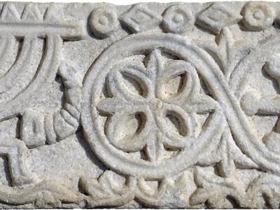 Stone relief featuring a candelabrum, horn, and plant bundle, floral patterns, and floral and geometric borders.