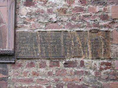 Photo of a weathered stone plaque with Hebrew inscriptions set into a rough brick wall.