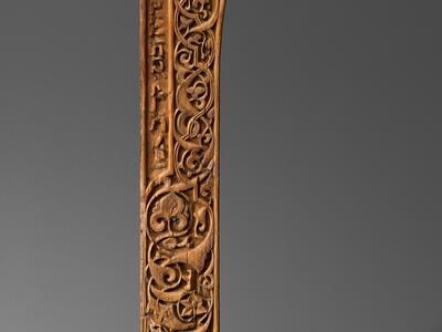Photo of a wooden architectural panel with a relief of intricate geometric and floral patterning and a line of Hebrew text down the left side.