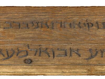 Rectangular mounted wooden plaque with two lines of carved Hebrew script.
