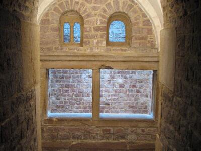 Photo of a stone stairway descending to an arched alcove with two arched windows above a larger rectangular window.
