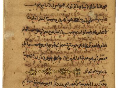 Manuscript page with nine lines of handwritten Arabic with red vowel markings, faint text between, and an ornate gold, red, and green floral decoration on the seventh line.