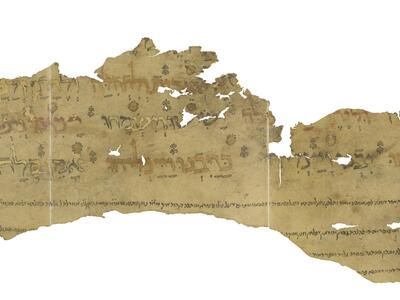 Irregular fragment of tattered manuscript with Hebrew lettering alternating between black, red, and gold, with vowels in black outline, and with small decorations disprersed among the words and smaller, vowelless lines of text below.