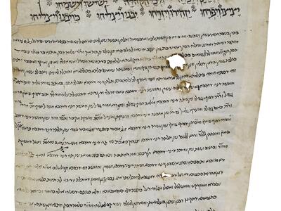 Damaged irregular manuscript page with large decorated Hebrew script at the top and smaller vowelless script below, conforming to the irregular shape of the page.