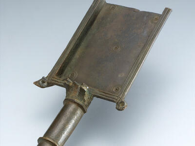 Ancient bronze shovel with a rectangular surface and a tapered cylindrical handle.