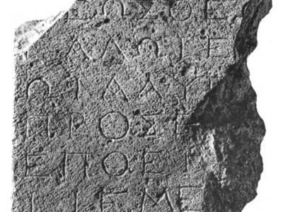 A stone fragment inscribed with ancient Greek text in several lines. The edges are irregular and broken.