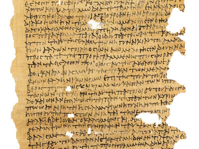 A fragment of an ancient papyrus document featuring lines of faded Greek script, with several lines in a Semitic script toward the bottom. There are visible holes, missing sections, and frayed, torn edges throughout the manuscript.