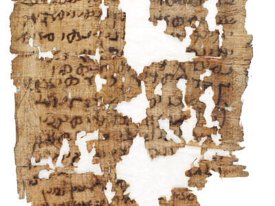 A fragment of ancient, damaged papyrus with faded black script in a Semitic language. Sections of the papyrus are missing.