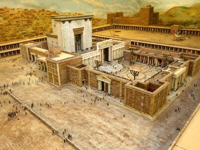 A detailed model depicts a temple, showing grand stone architecture, columns, courtyards, and miniature figures representing people in an ancient city setting.