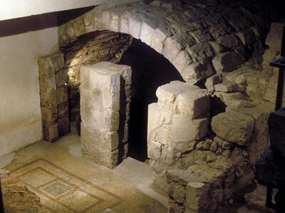Stone archway surrounded by partially built stone structures, with tile mosaic visible on the floor next to the archway.