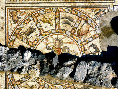Mosaic with three registers, arranged vertically. In the center register is a depiction of a person with a halo surrounded by the zodiac. In the top register is a Torah shrine flanked by two menorahs, surrounded by ritual objects. In the bottom register is a grid with Greek inscriptions, flanked by lions.