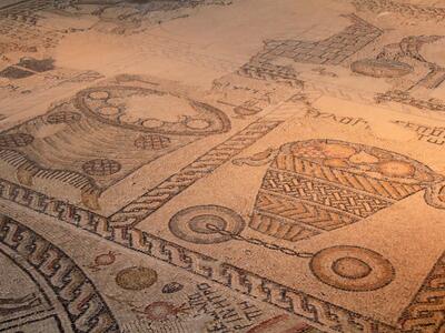 Ancient mosaic floor showing a basket filled with fruit with two birds hanging off it, and other items, surrounded by decorative borders.