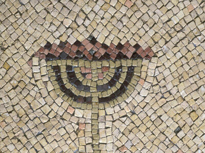 Ancient mosaic depicting a menorah with seven branches made from colored tiles, set against a beige background with geometric patterns.