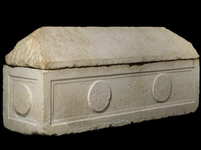 A rectangular stone sarcophagus with a pitched lid, featuring carved circular decorations on its sides.