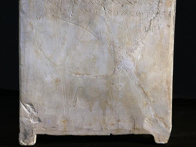 Side view of a stone ossuary featuring an inscription in Greek letters. The inscription is also transcribed below in clear handwriting.