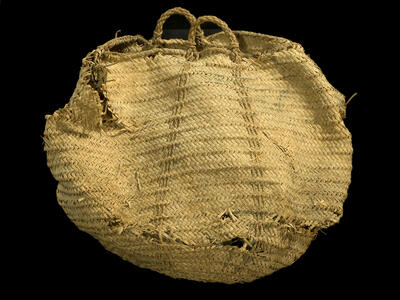 A large, round woven basket made of natural fibers with two handles, displaying signs of wear and some fraying along the edges.
