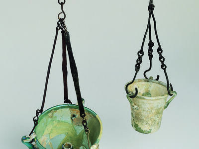 Two ancient greenish, bucket-shaped glass lamps hanging against a plain background.