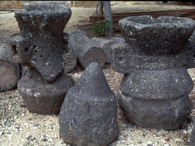 Several large, weathered grindstones are grouped outdoors on gravel.
