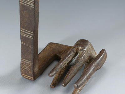 A metal object with a vertical handle featuring etched lines, attached to a flat base with five prongs at the end resembling a claw.