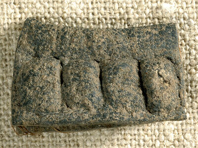 A rectangular, weathered artifact with four raised, rounded sections sits on coarse fabric.