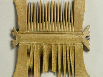 A double-sided, ancient wooden comb with wide teeth on one side and fine teeth on the other, showing some broken and uneven teeth.