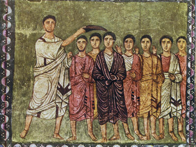 A painting shows a figure in a white robe anointing the head of another figure standing among several others, all dressed in robes, against a background with a decorated border.