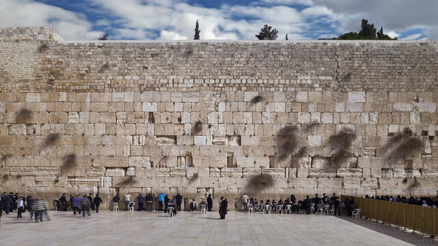 Photograph of large stone wall with many people in front praying.