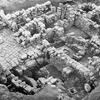 Aerial view of stone ruins, showing multiple rectangular rooms and passageways with uneven stone walls and floors, partially surrounded by earth and vegetation.