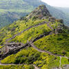 Ruins of an ancient stone fortress with winding walls built along a lush, green hillside.