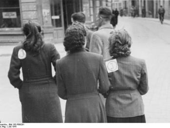 Photo of three Jewish women wearing badges identifying them as Jewish, in the Vilna ghetto.
