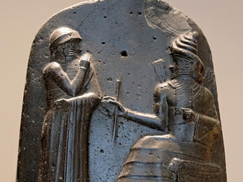 The top of Hammurabi's Stela; Hammurabi stands with a hand to his nose in submission to the seated god Shamash.