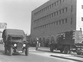 Black and white photo of mid-20th-century city street with an automobile and buildings in the background.