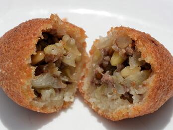 Photograph of a fried kibbeh cut open to reveal the meat filling.