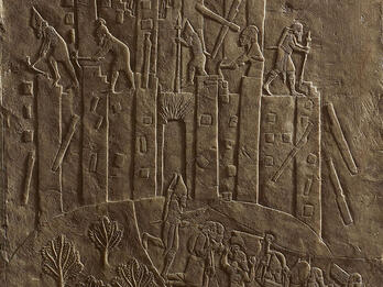 Relief of building with figures on top and below carrying objects. 