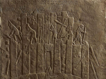 Relief of building with figures on top and below carrying objects. 