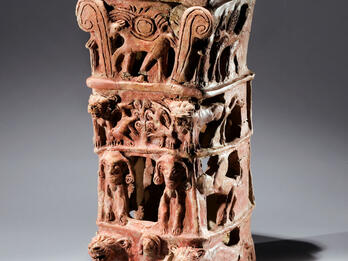 Ceramic Offering Stand from Taanach Ceramic offering stand with flat top and four layers of decoration: bottom layer of nude female with raised arms flanked by lions, second layer of two winged figures, third layer of goats eating leaves off tree, and fourth layer of four-legged animal with winged sun disk and palm fronds.