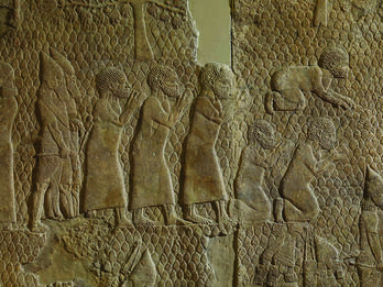 Men Doing Obeisance to Sennacherib Wall relief showing six men dressed in tunics, one prostrate and two kneeling, with two bearded soldiers behind them.