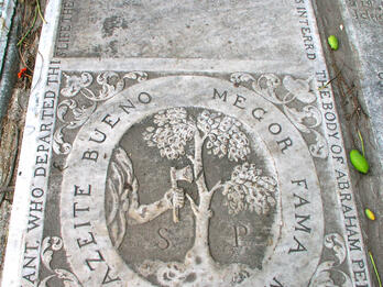 Gravestone of Abraham Pereira d’Azevedo Tombstone with Latin inscription on top half and illustration below of axe chopping tree in half, surrounded by English words around perimeter of stone.