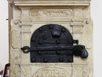 Alms Box Carved wall unit with decorative borders and crowns, locked metal box in middle, and Hebrew text underneath.