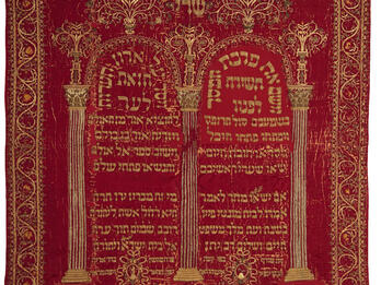 Torah Curtain Cloth embroidered with Hebrew writing under columned archway and surrounded by decorative border.