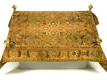 Carpet with embroidered designs and four small posts near each corner. 