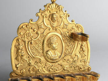 Hanukkah Lamp (France) Oil lamp in the form of a shield with spouts at the bottom, of decorative motifs and profile of individual crowned with laurel wreath.