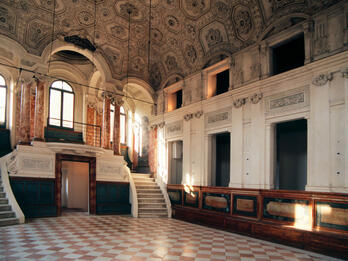 Sephardic Synagogue, Pesaro, Italy Interior of room with columns and short double staircase at one end and pews along wall.