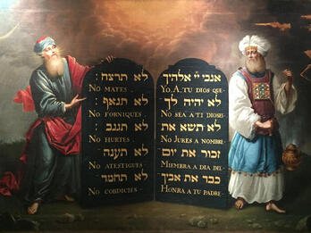 Moses and Aaron with the Ten Commandments Painting of two bearded men in robes, one on each side of large tablets with Hebrew and Spanish text.