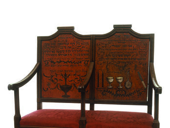Circumcision Bench Two-seater bench with central armrest, decorated on the seat backs with ritual objects and Hebrew text.